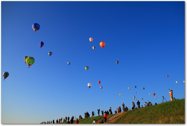 青空に上がる気球を見上げる人々のシルエット